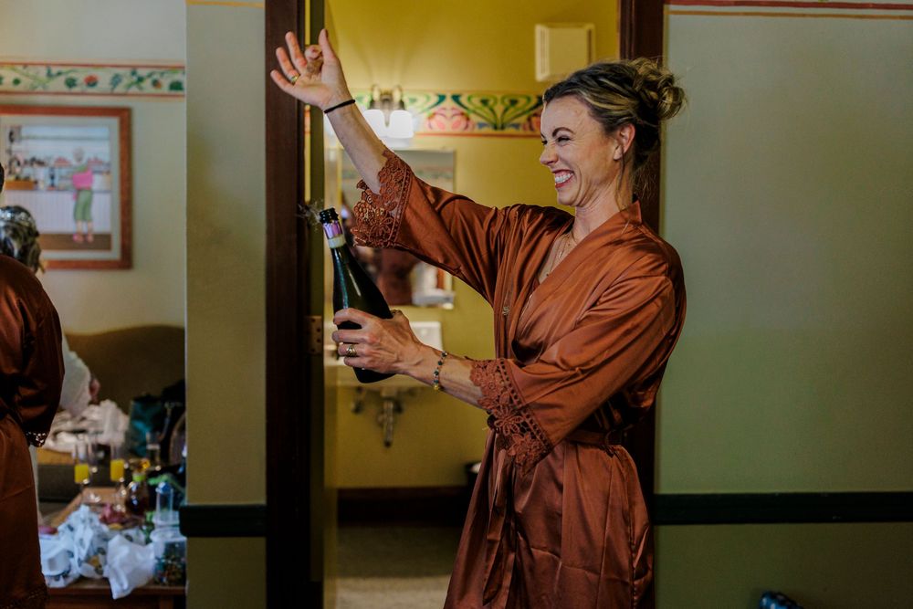 A figure in a copper-colored silk robe raises their arms in celebration during wedding preparations.