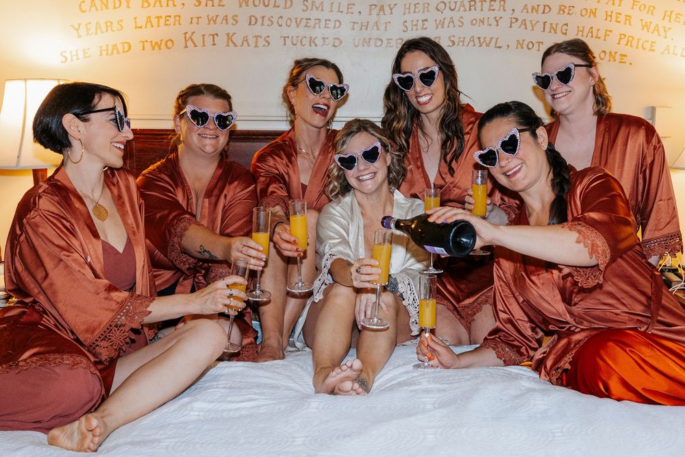 Wedding party in rust-colored robes toast and celebrate during pre-ceremony preparations.