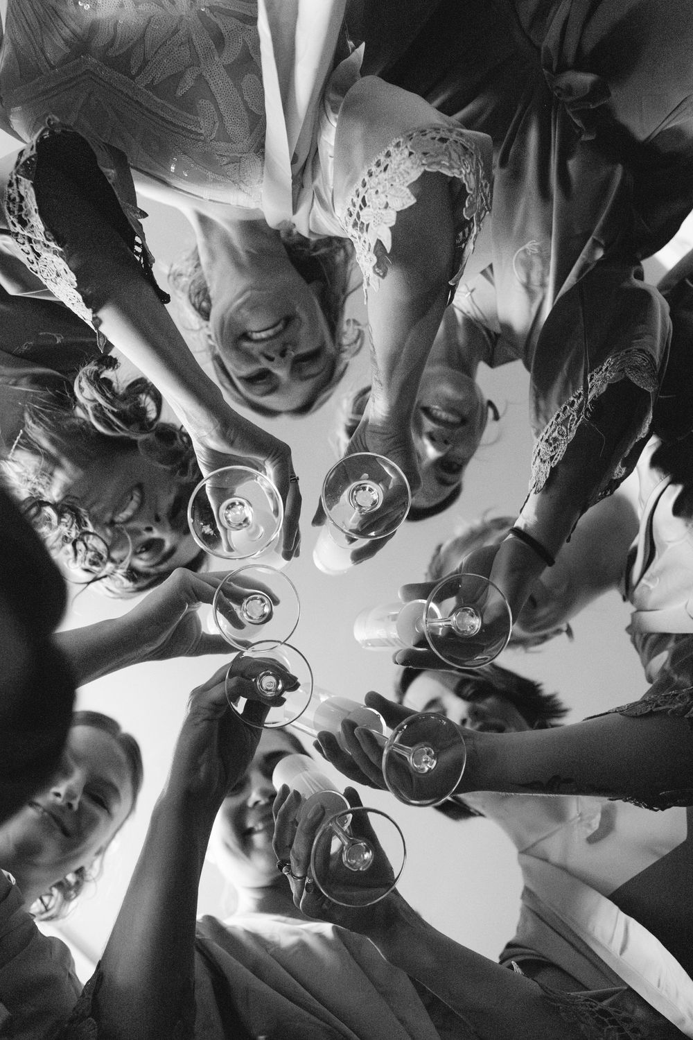 A black and white overhead view of people in a circle toasting with champagne glasses.