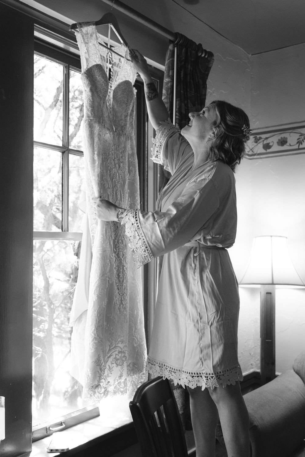 A row of elegant white wedding dresses hanging by windows in black and white photography.