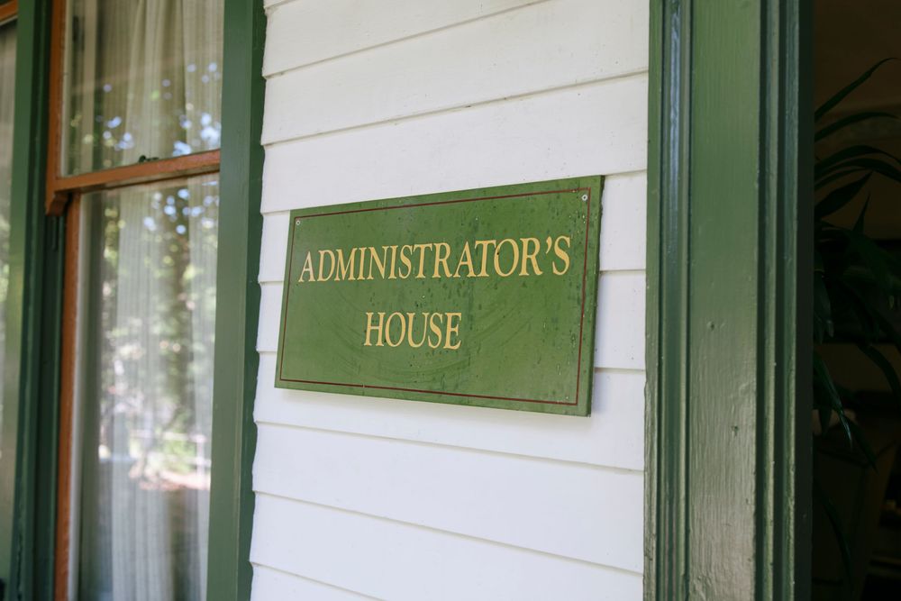 White building exterior with green trim and gold lettering showing 'Administrator's House' signage.