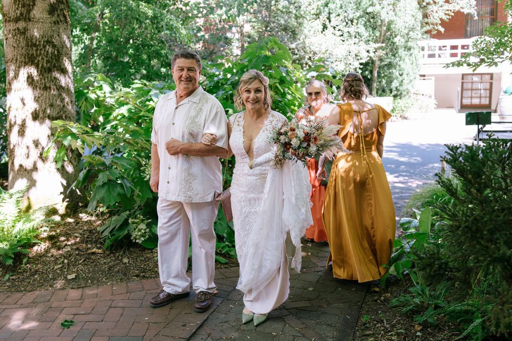 A group walking together outdoors in light colored and gold attire among trees and brick paths.