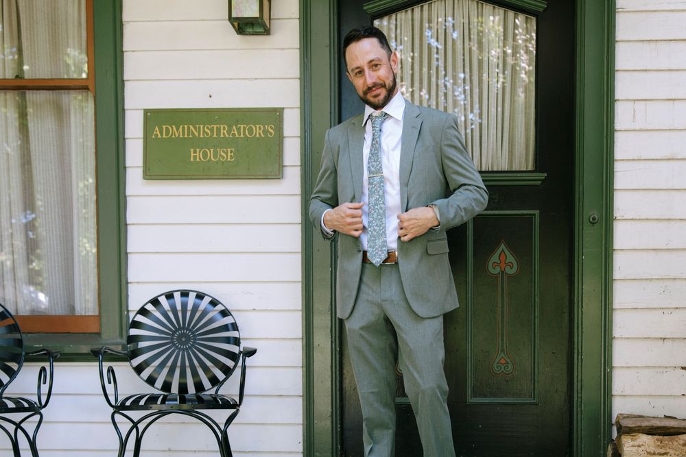 Groom in grey suit standing by door marked Administrator's Park.