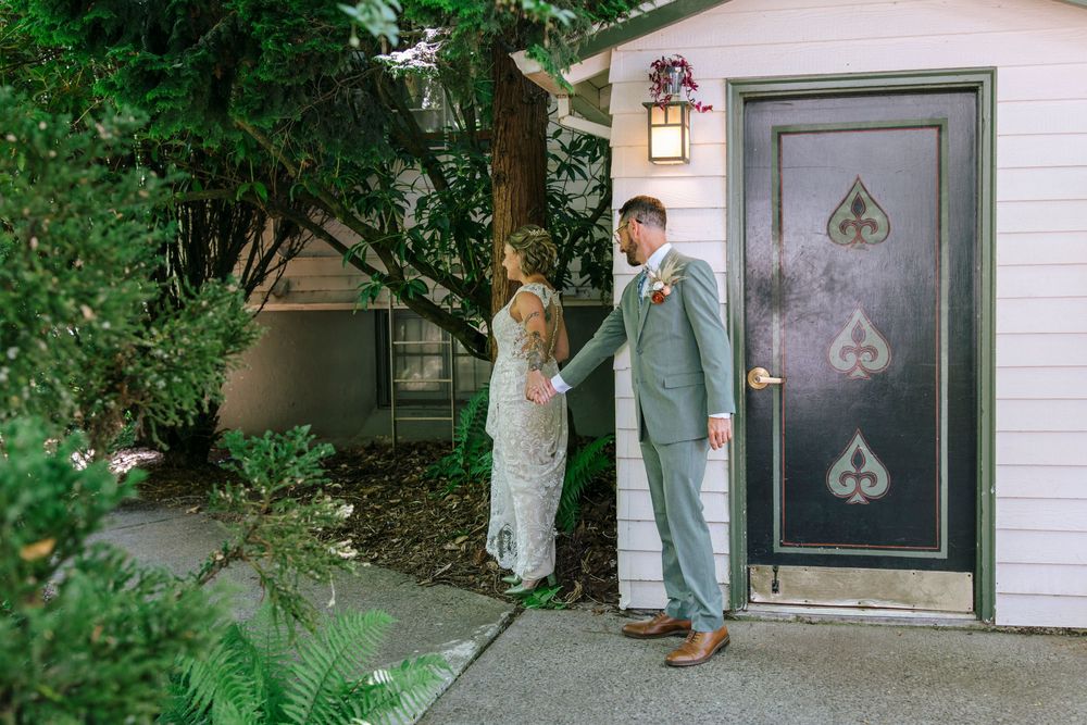 Wedding photos by a white garage door with spade symbol, surrounded by greenery and trees.