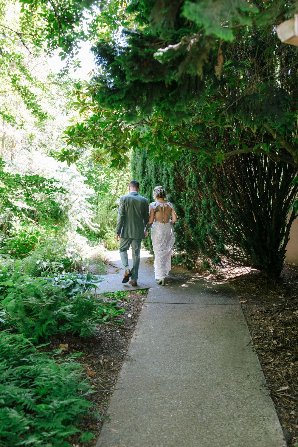 Wedding couple walking along a garden pathway surrounded by lush green vegetation.