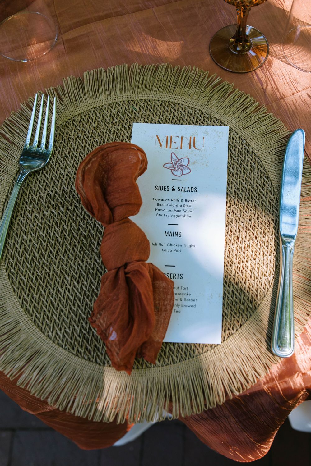 Wedding reception place setting with rustic woven placemat, terracotta napkin and elegant menu card.