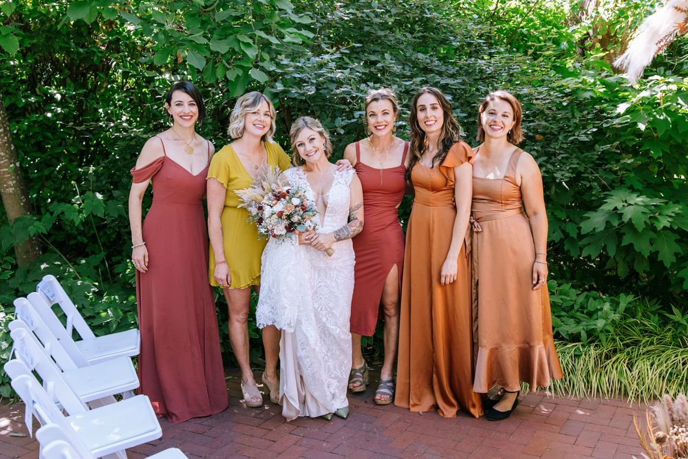 Wedding party in earth-toned dresses and suits poses together in a lush garden setting.