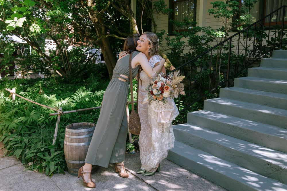 Two people embrace on outdoor stone steps surrounded by lush greenery, with one wearing a sage green dress and another in lace.