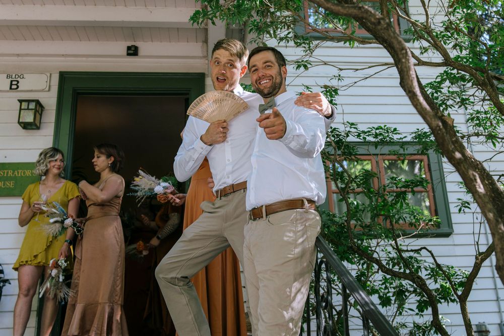 Candid outdoor reception celebration with guests mingling on a porch of a white house surrounded by greenery.