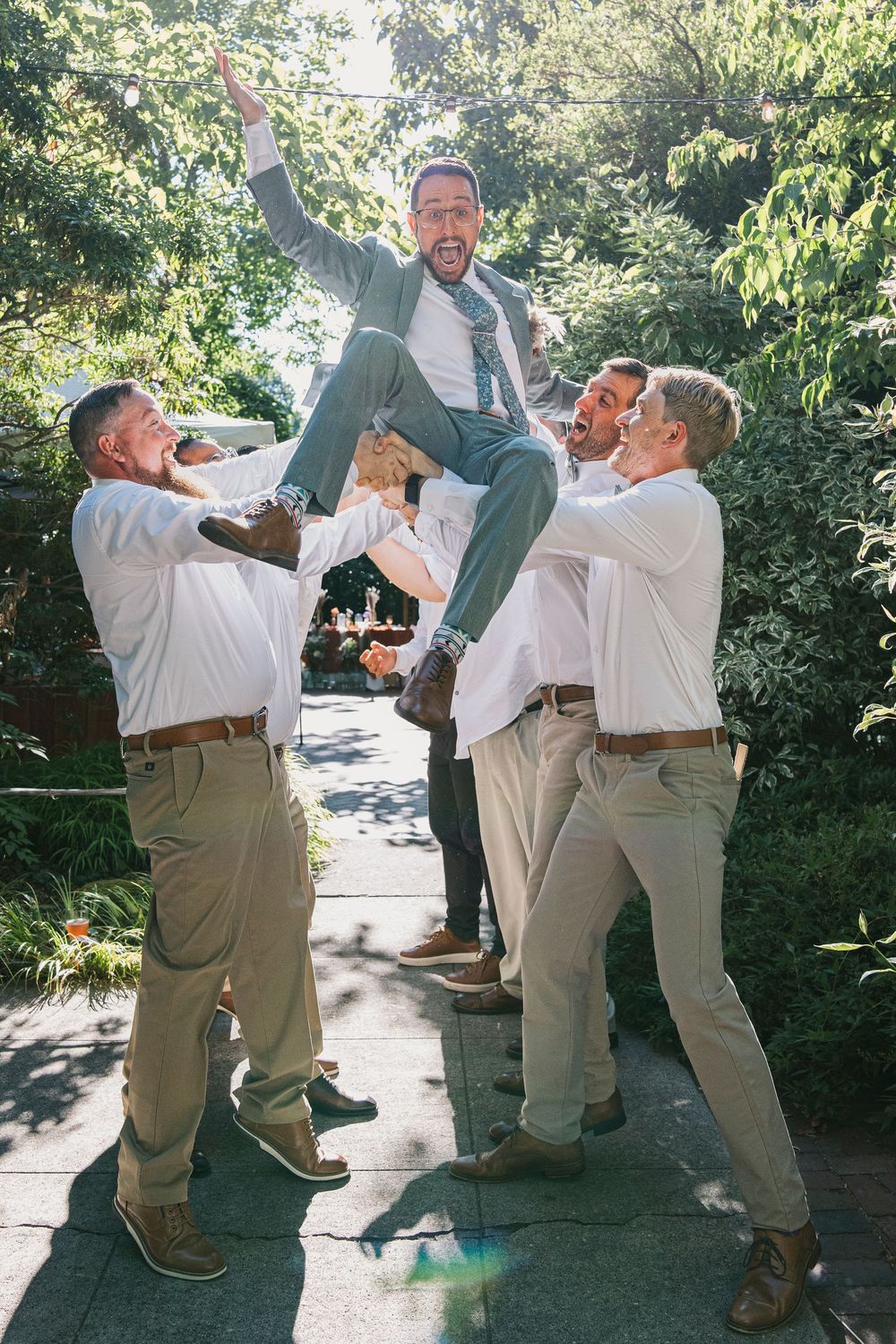 Groomsmen performing a playful sequence with champagne bottles at an outdoor wedding celebration.