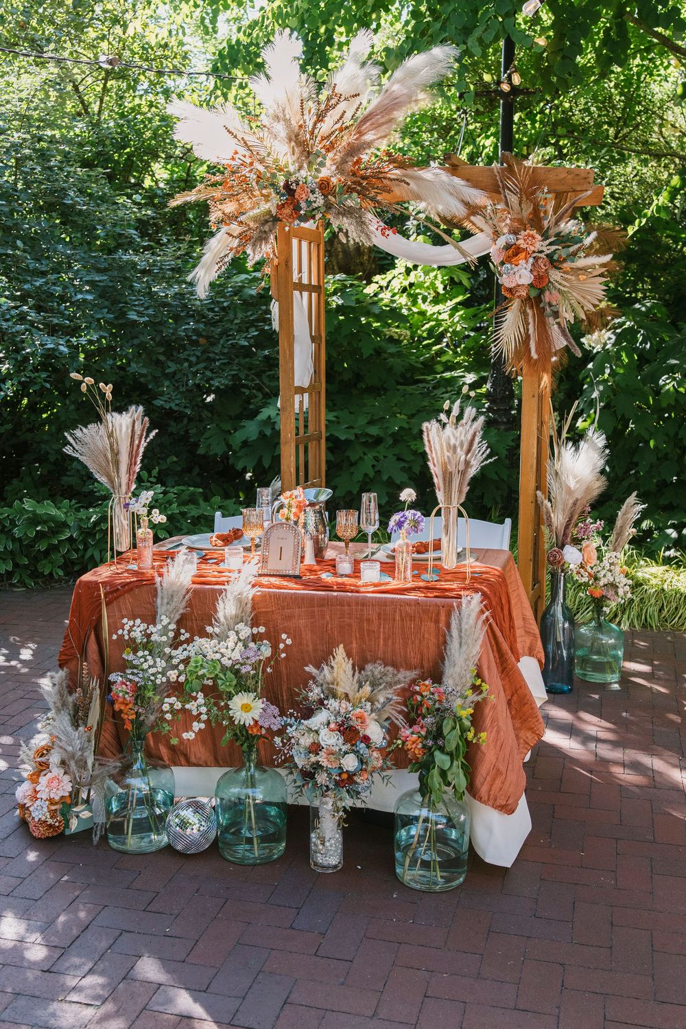 Rustic wedding decor featuring dried flower arrangements in mason jars on brick patio.
