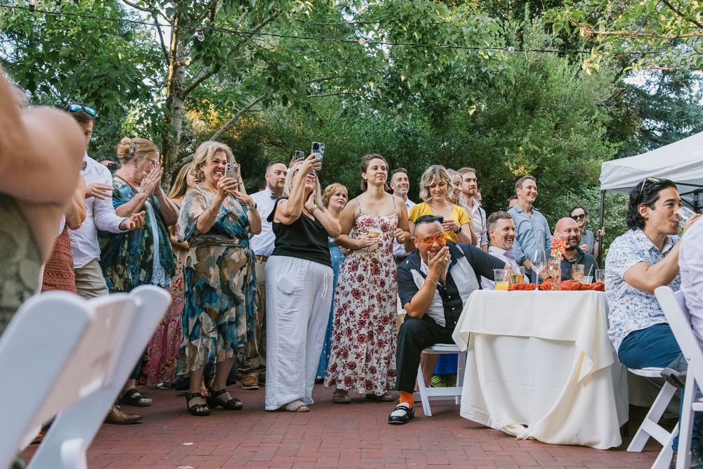 Wedding guests react excitedly during an outdoor reception celebration.