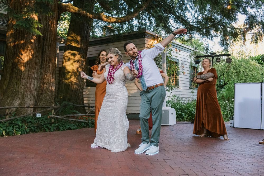 A joyful wedding celebration on a brick patio with people dancing and posing together in front of trees.
