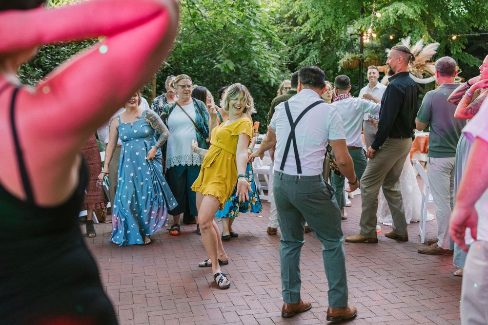 Wedding guests dance together on an outdoor brick patio during a summer celebration.