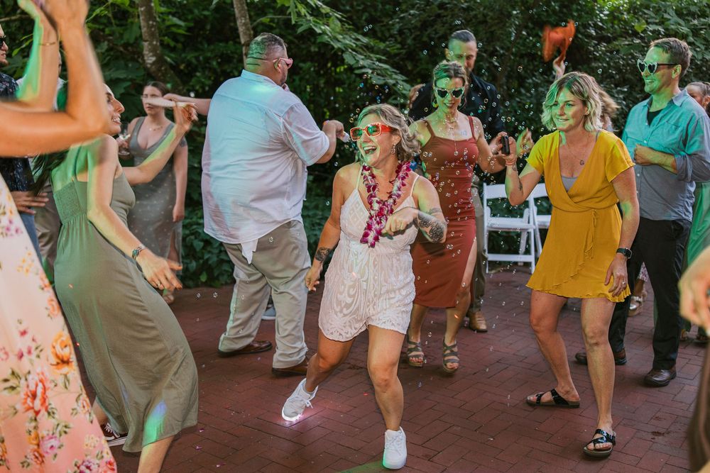 A large group of people dance together outdoors on a brick patio during a festive celebration.