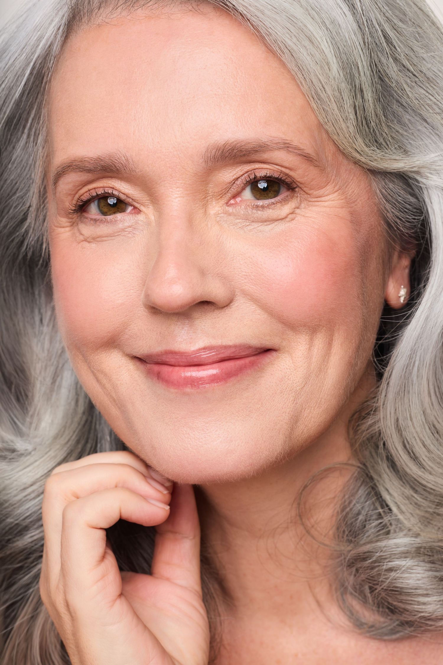Close-up beauty portrait of a smiling mature woman with wavy silver hair and glowing skin.