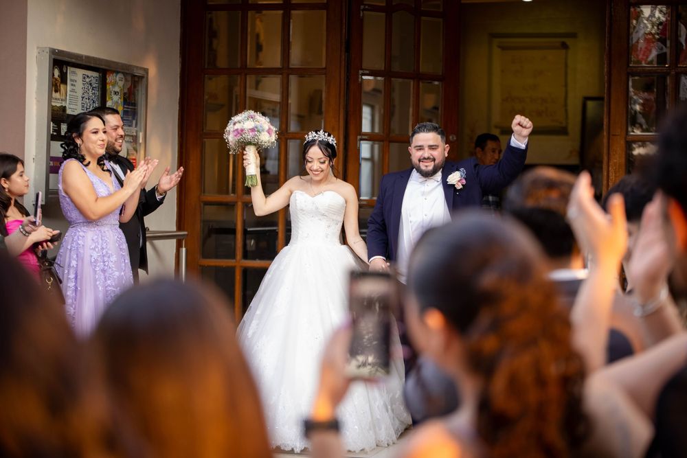 Wedding celebration with guests cheering as couple celebrates in church entrance.
