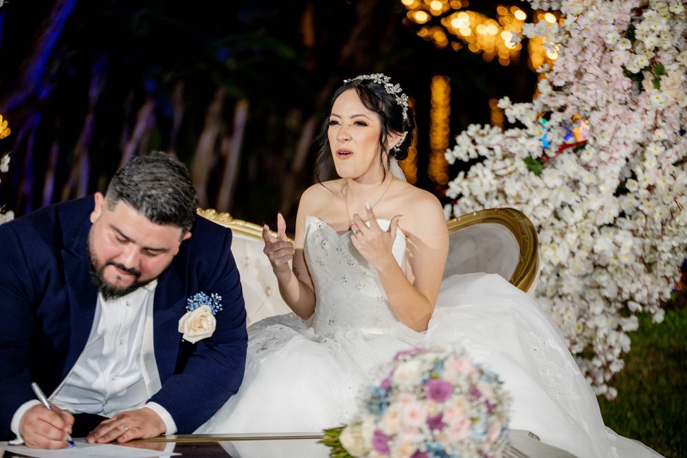 Couple signing marriage documents at elegant wedding ceremony with floral arch and romantic lighting.