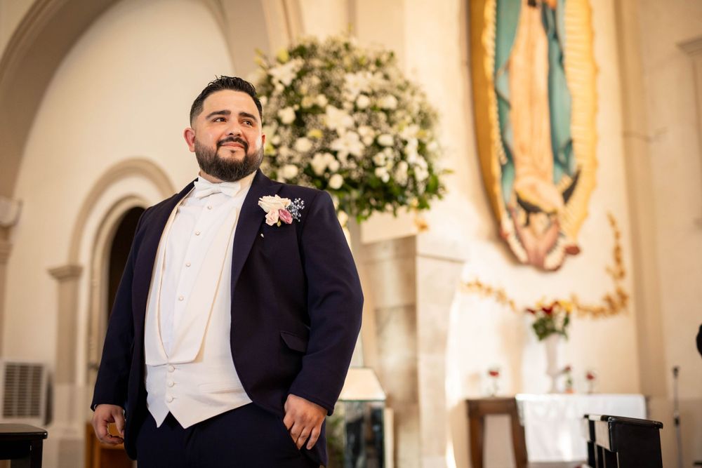 Groom in formal navy suit stands in ornate church interior.