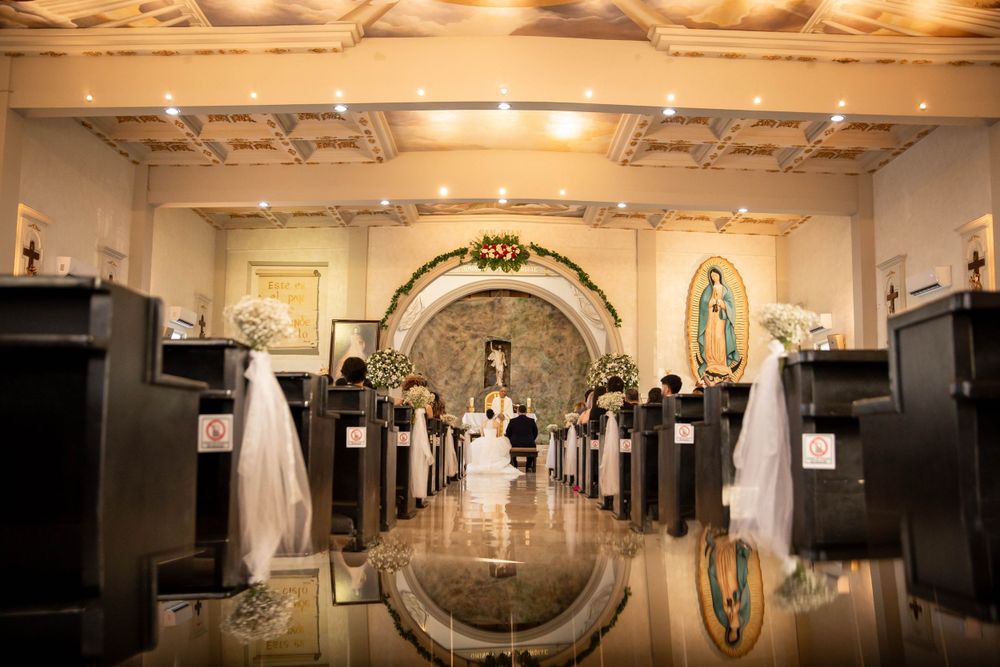 Ornate Catholic church aisle with white decorations and polished floors creating a mirror reflection for a wedding ceremony.
