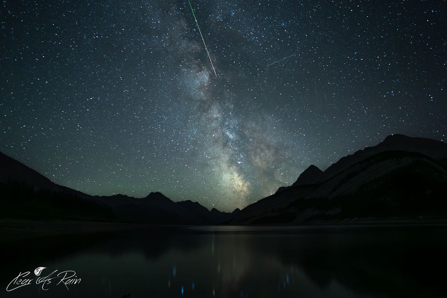 Stunning night sky showing the Milky Way galaxy and shooting star reflected in a mountain lake.
