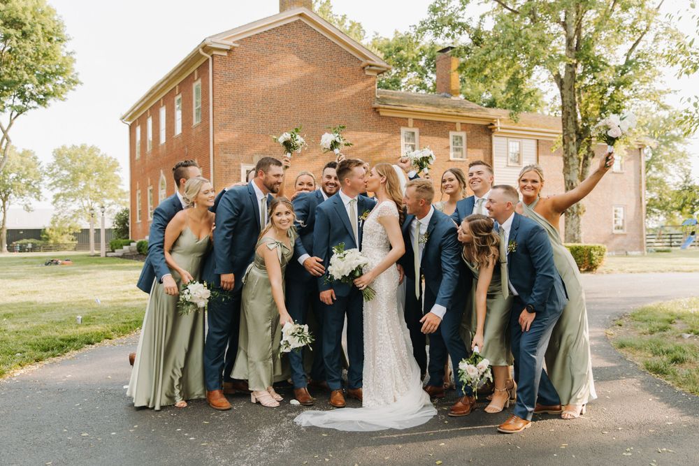 A wedding party poses together on a path in front of a red brick building on a sunny day in Lexington, Kentucky.