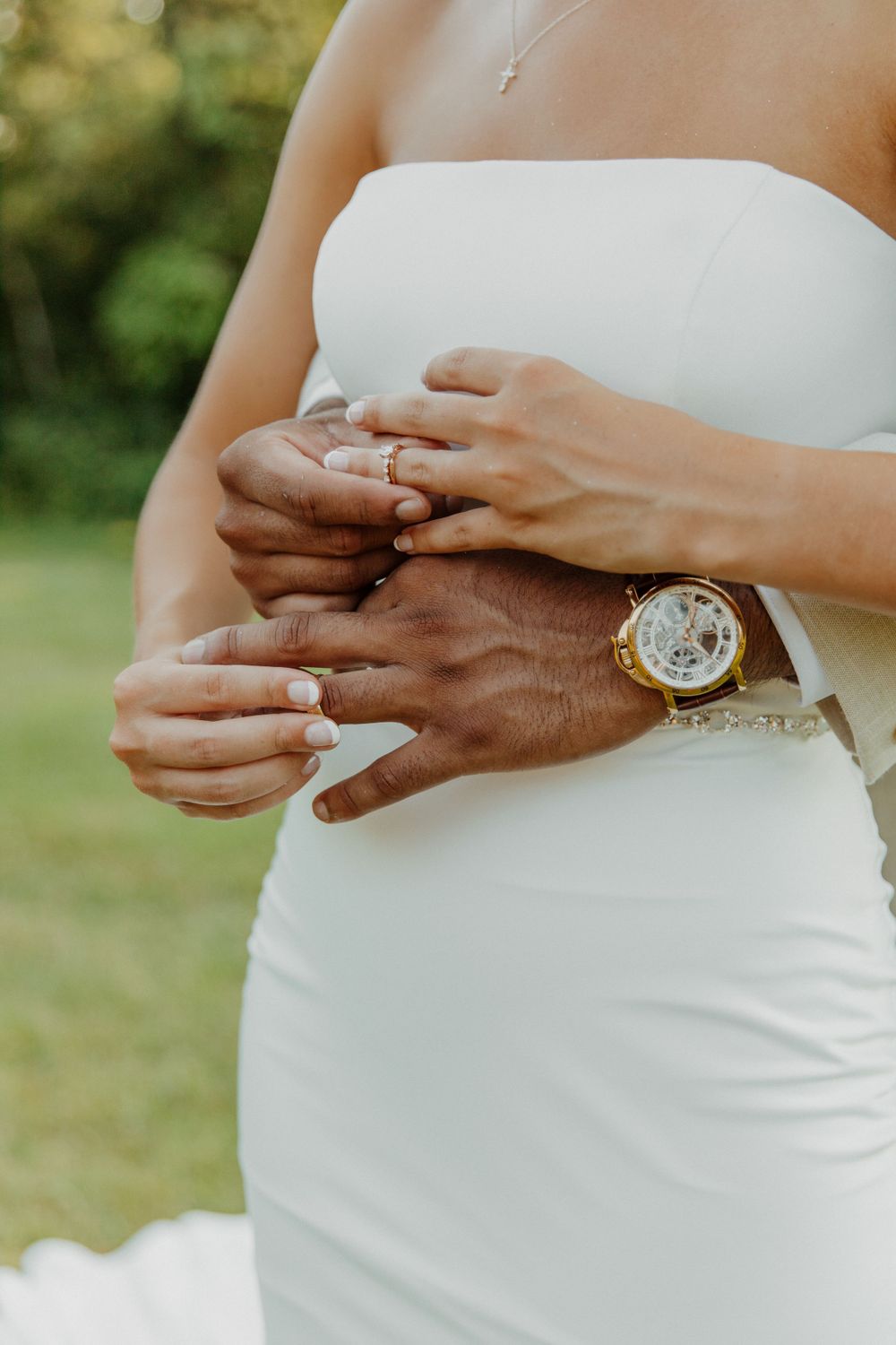 Close-up of hands exchanging wedding rings, with one person wearing a white dress and the other wearing a gold watch.