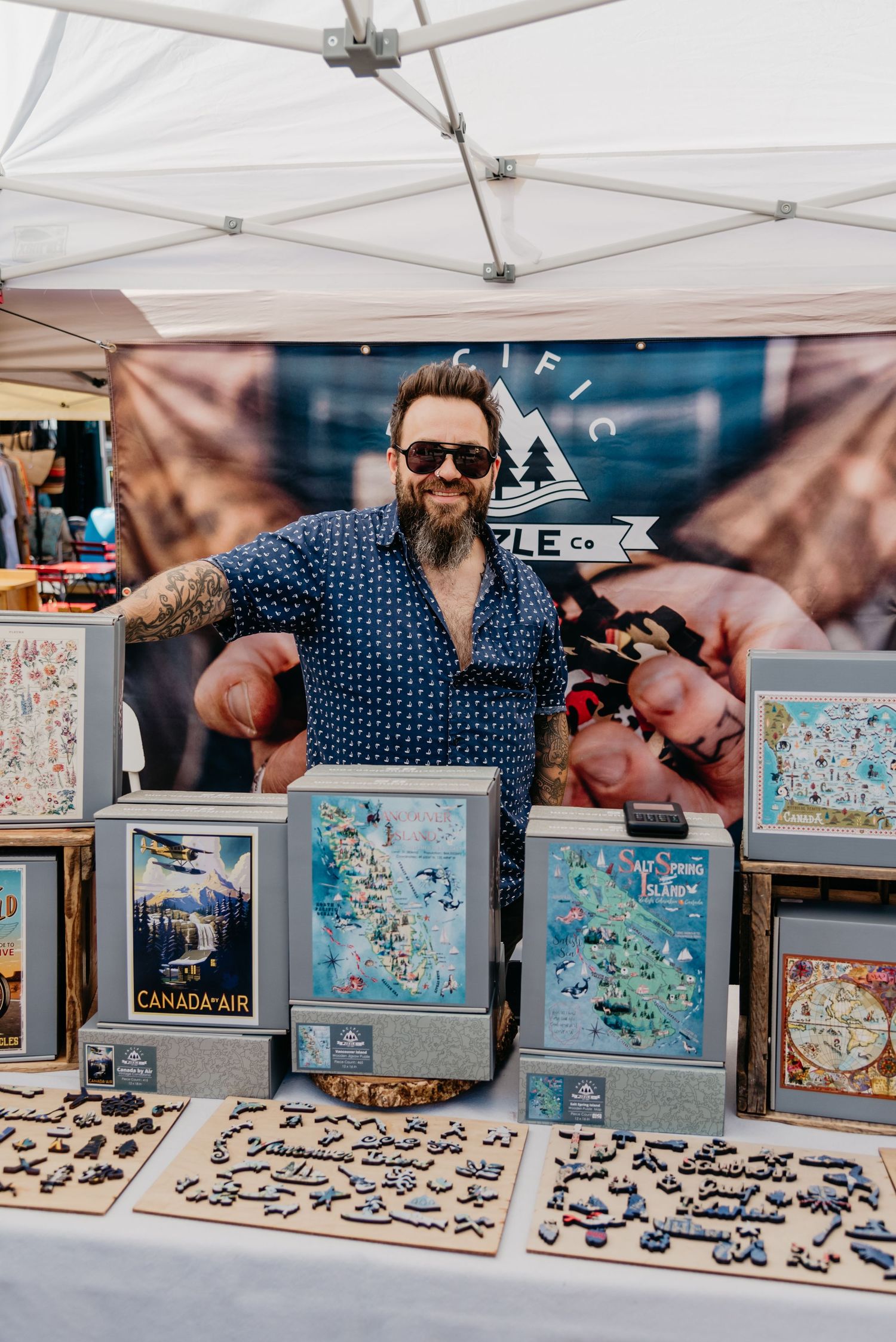 Canadian puzzle maker Aaron stand with his wooden puzzles at vendor booth on Salt Spring Island, BC, Canada