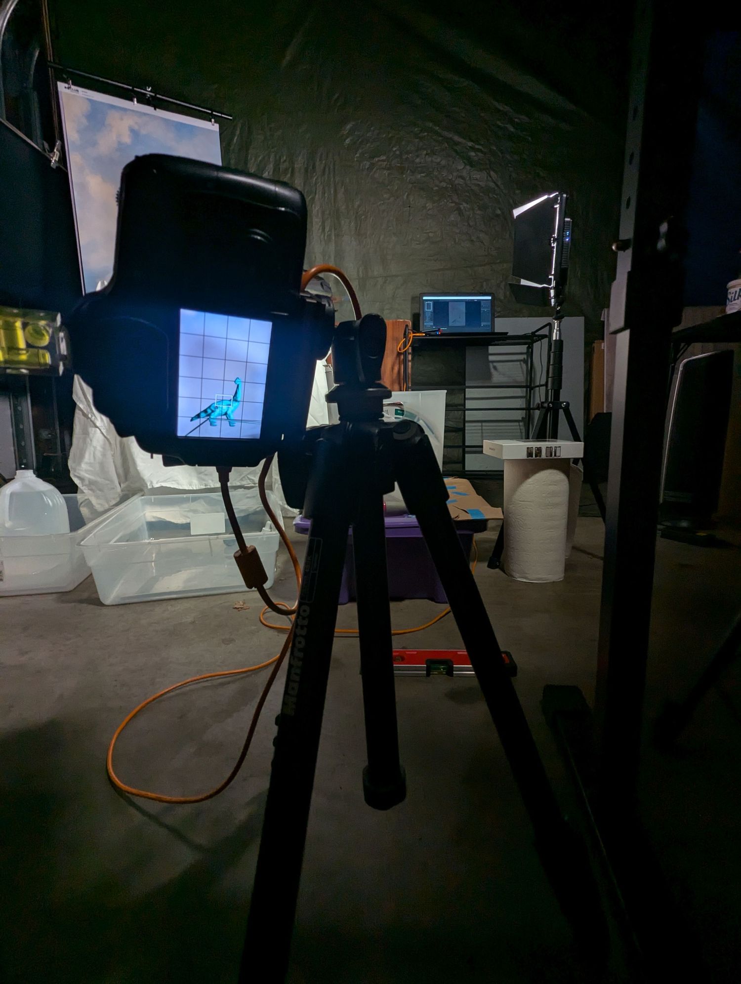 Camera equipment mounted on a tripod with scene displayed on screen and cables visible in a studio setting.
