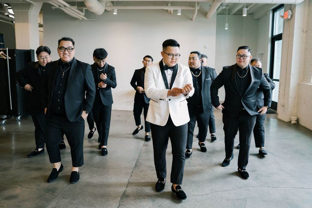 A stylish groomsmen group poses in a modern indoor space wearing black suits.