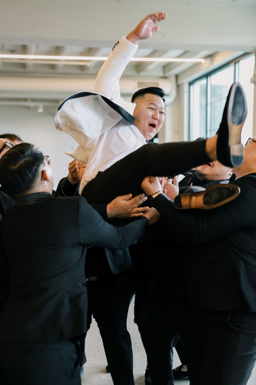 Joyful wedding party members lifting and celebrating in a candid moment during indoor photo session.
