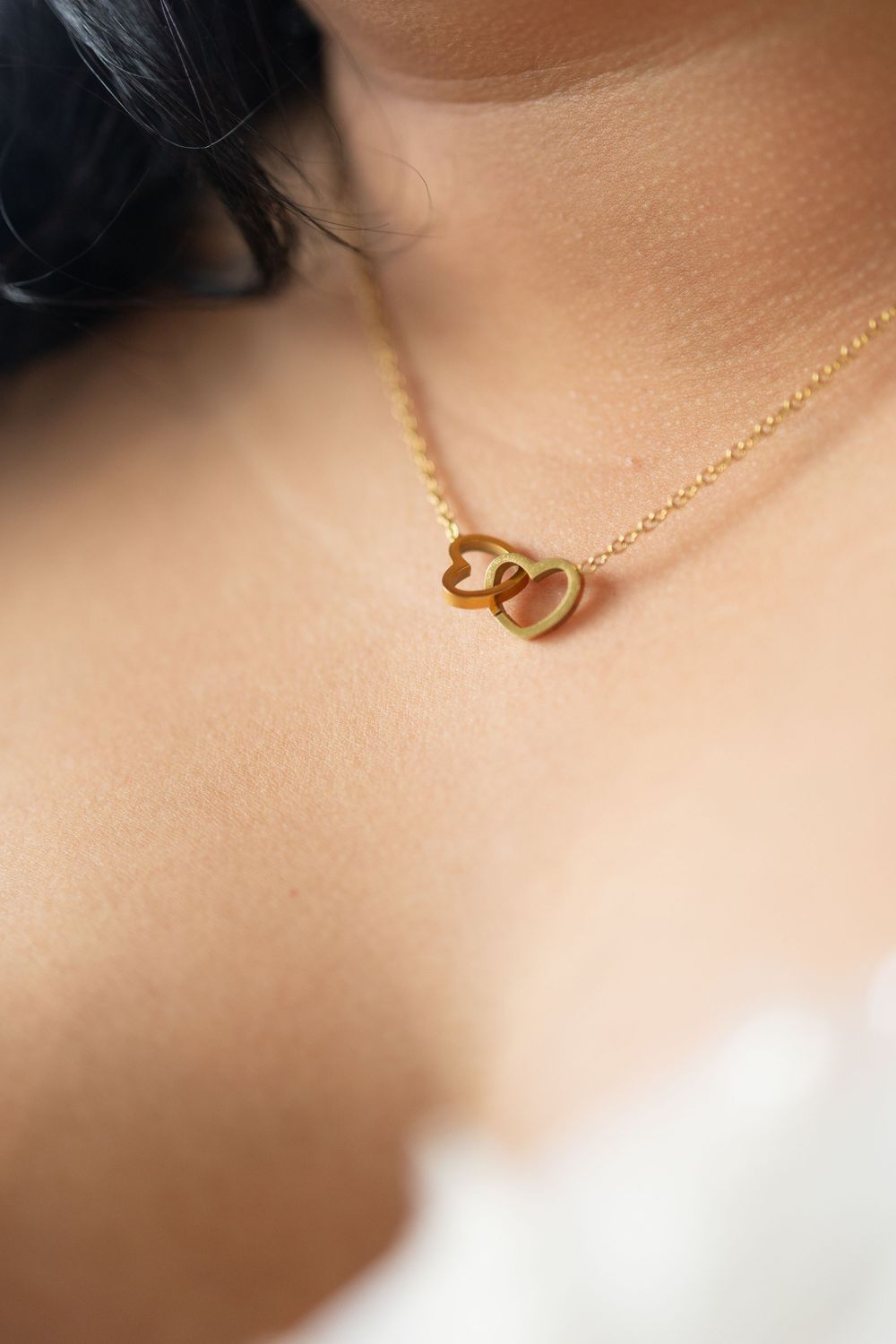 Delicate gold necklace featuring interlocking heart charms on a fine chain displayed against soft skin.