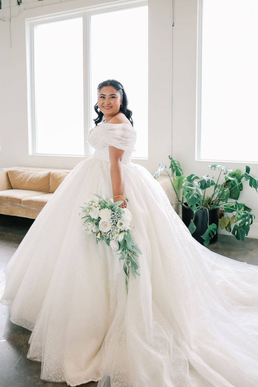 A bride wearing an elegant off-shoulder ball gown wedding dress holds a cascading eucalyptus and white flower bouquet.