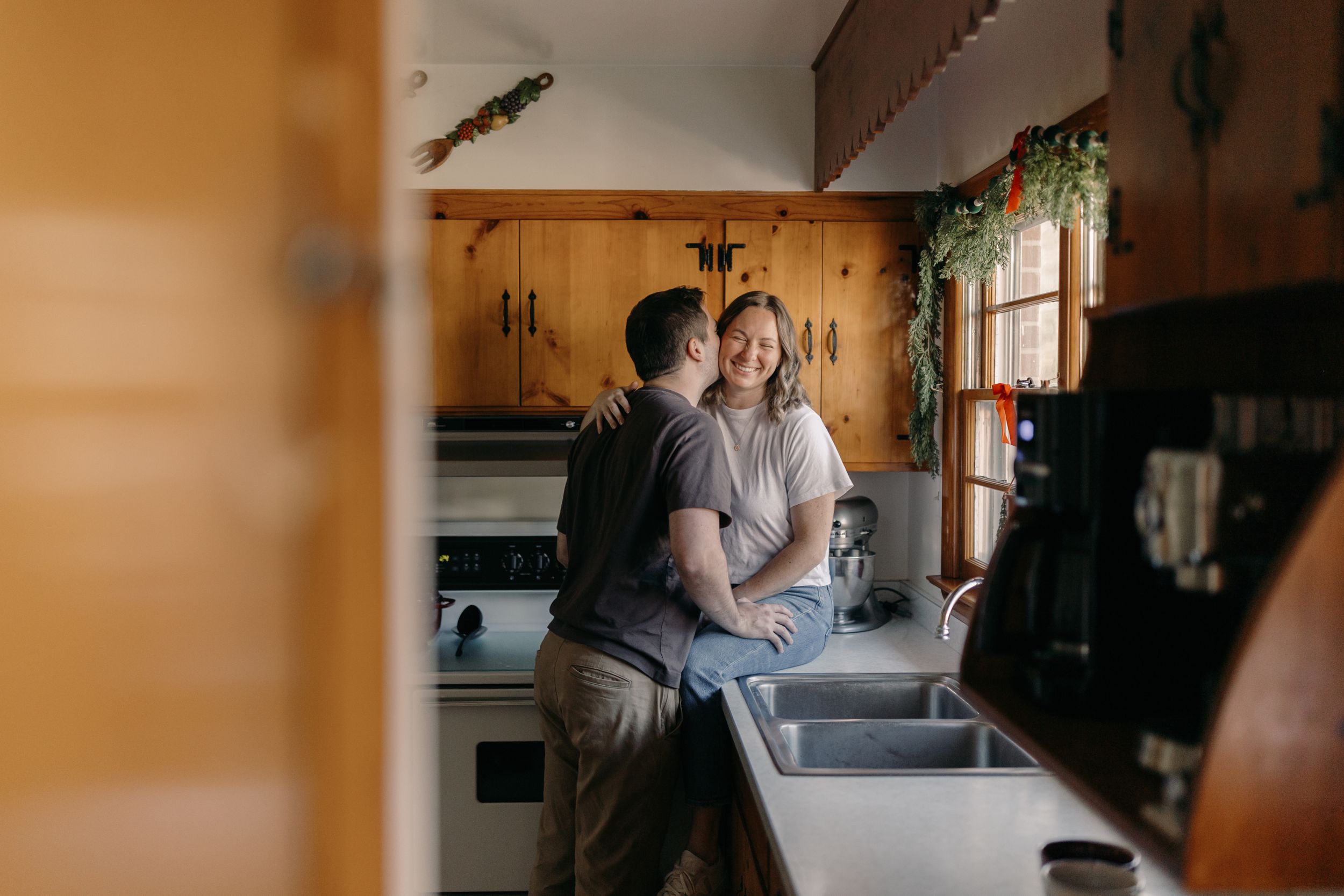 A couple shares a tender moment in their kitchen while leaning against the counter.