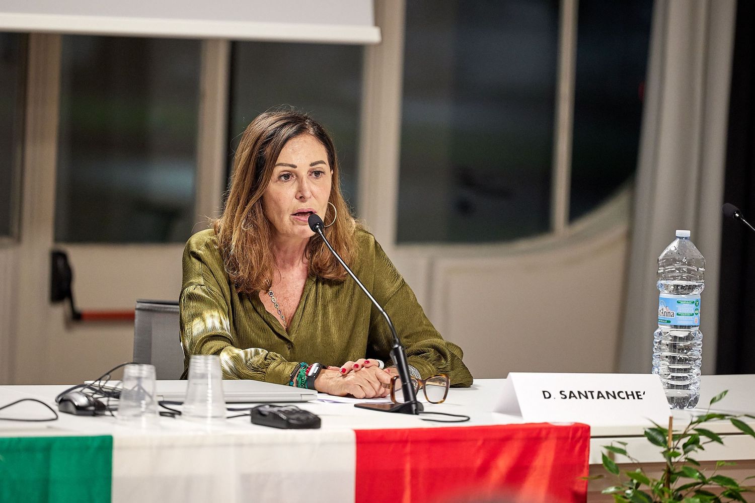 Conference speaker at table with microphone and water bottle.
