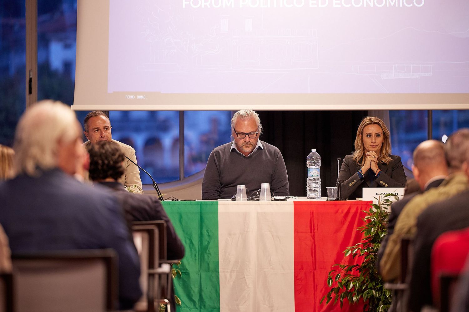 Conference panel with Italian flag tablecloth speaking to seated audience.