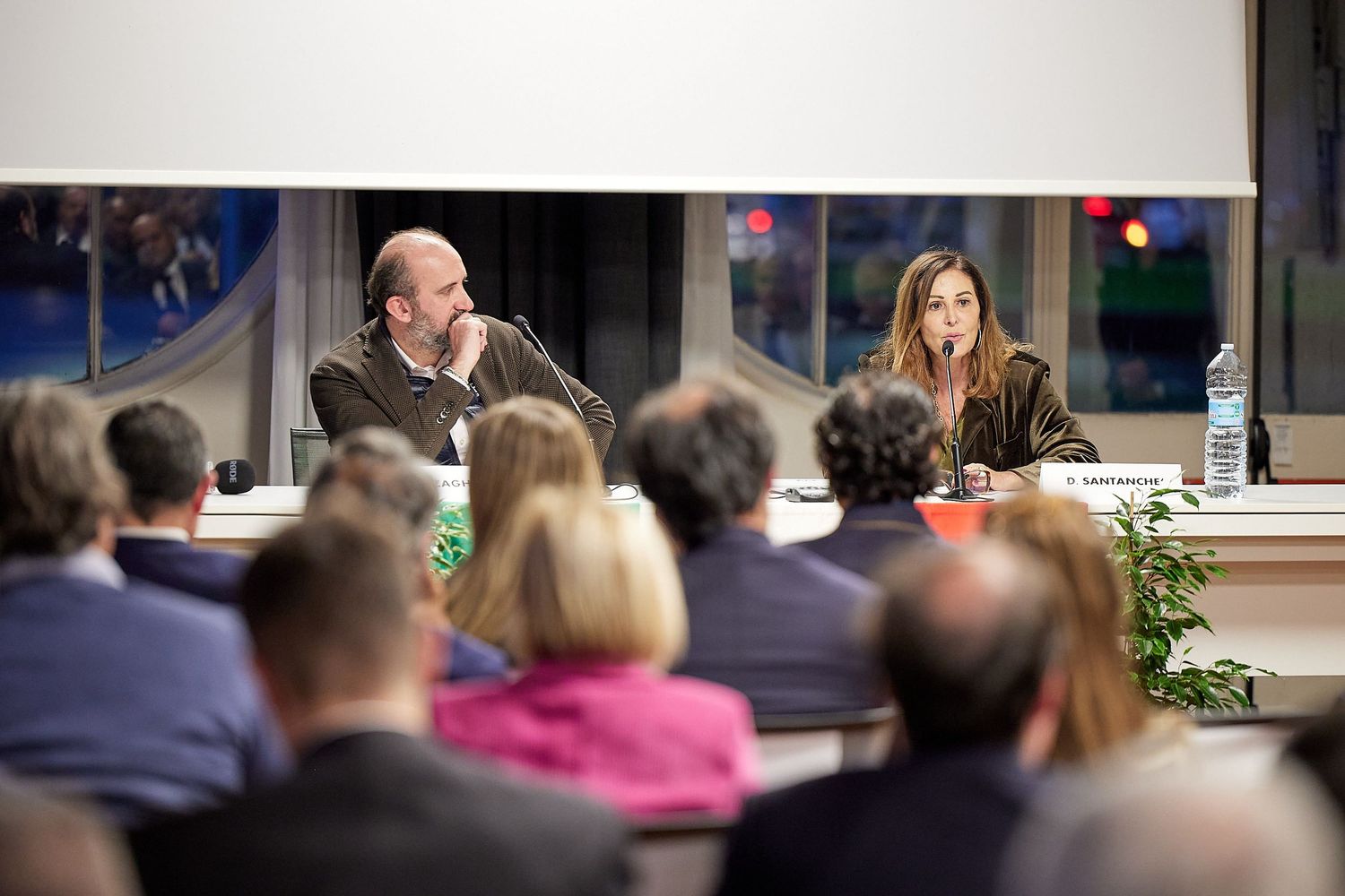 A presentation or lecture taking place with speakers at a table addressing an audience in a conference setting.