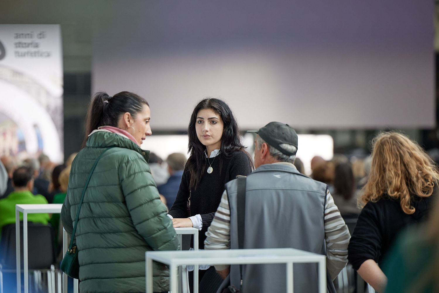 People gathered around a white table having a discussion at an indoor event.