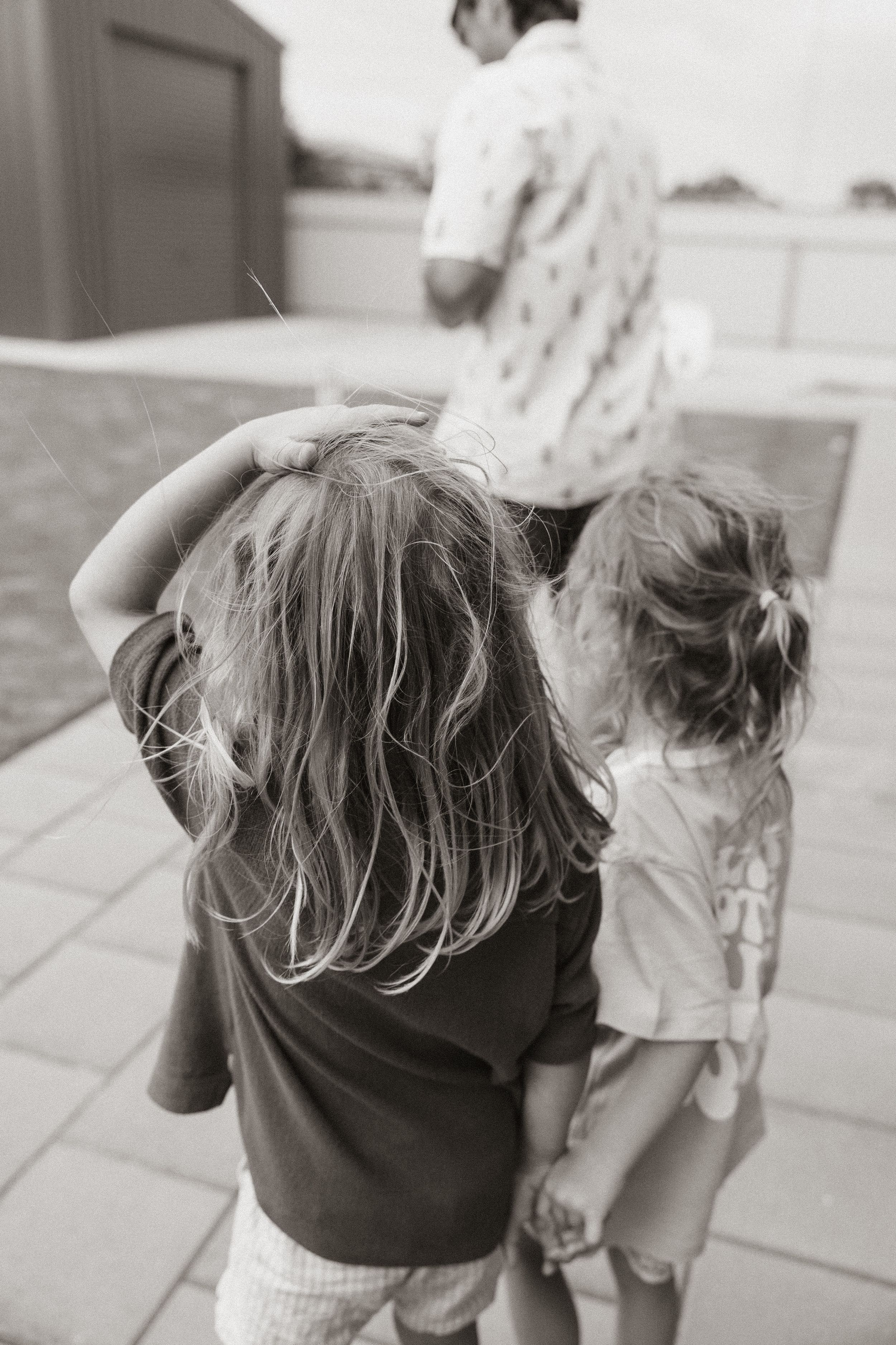 Two young children stand together outdoors in black and white, photographed from behind.
