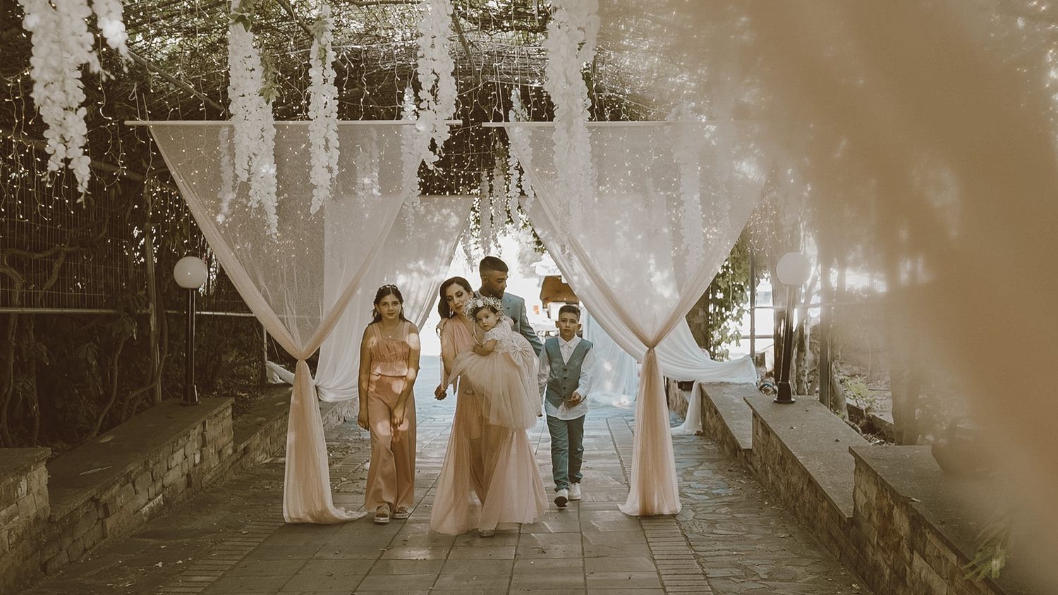 A romantic wedding ceremony takes place outdoors at dusk with flowing white fabric draping and soft lighting.