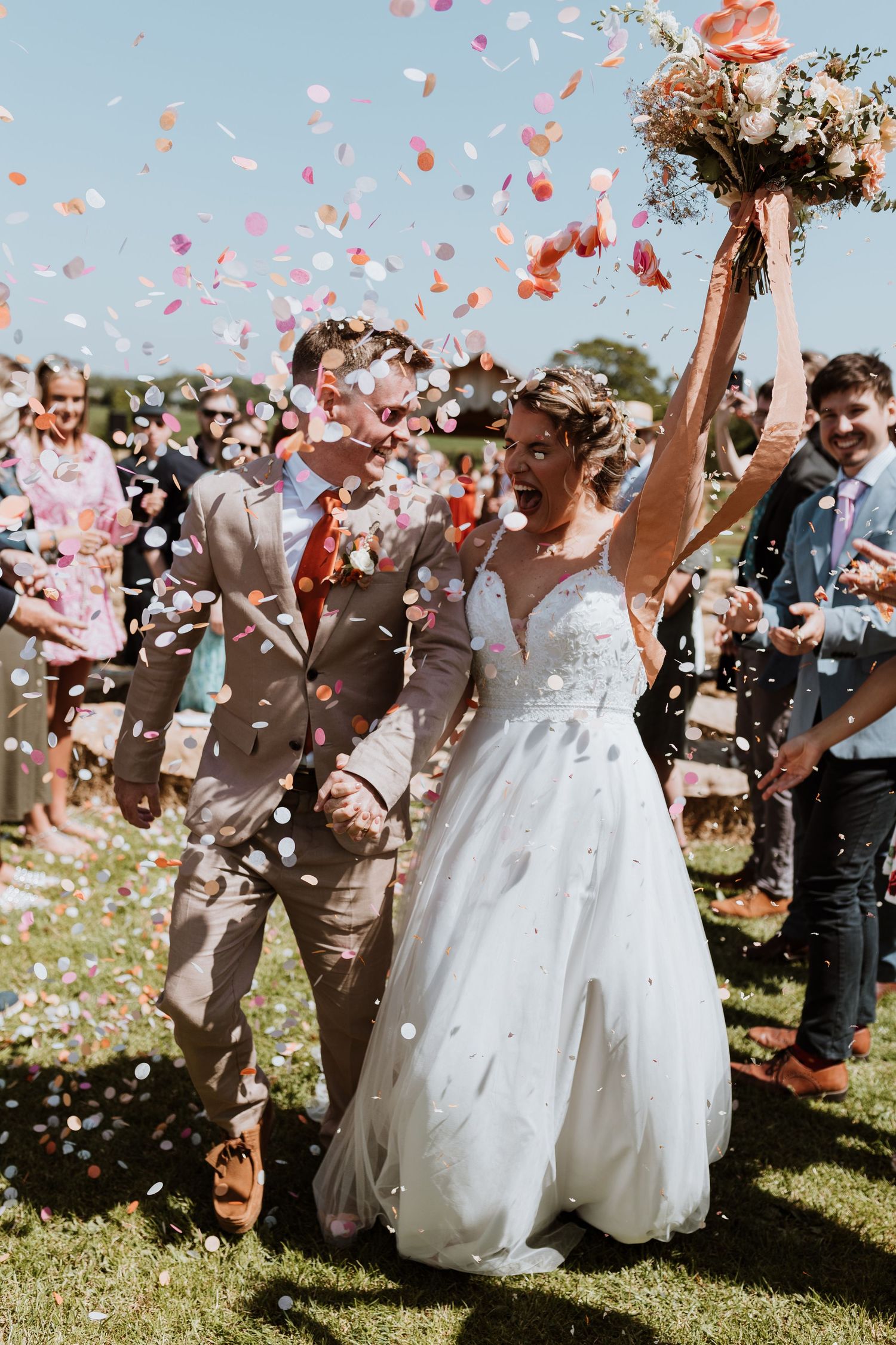 Newlyweds celebrating under a shower of pink and coral confetti petals during outdoor garden wedding ceremony.