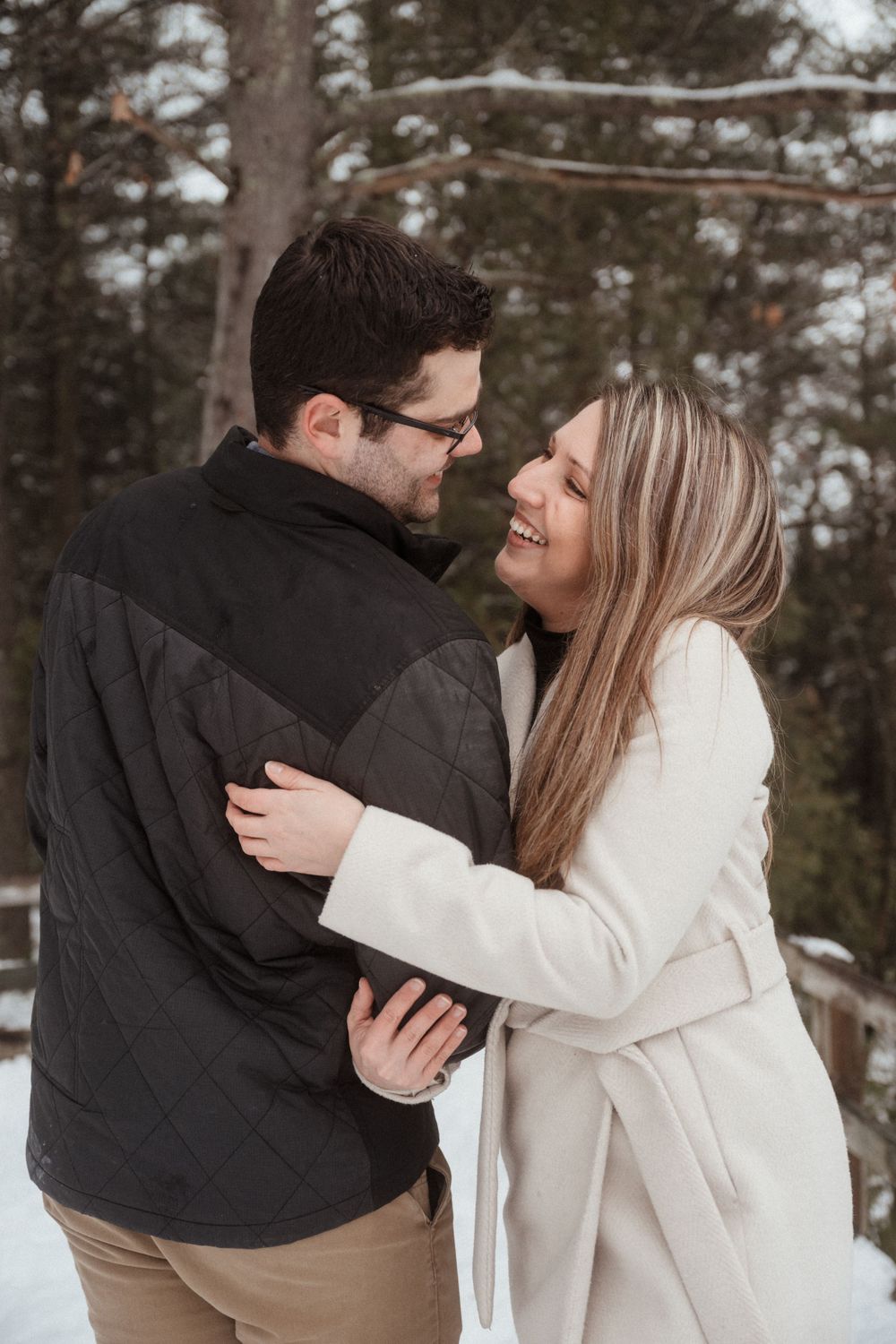 A couple shares a loving embrace on a snowy winter day in the woods.