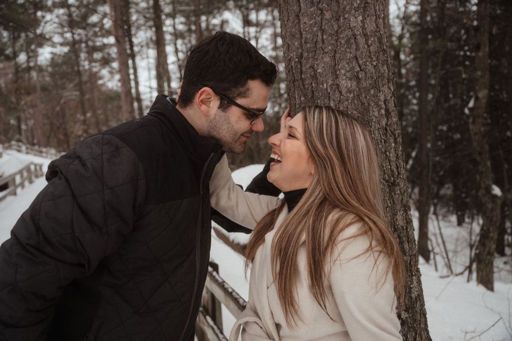 A romantic winter photoshoot of a couple sharing an intimate moment against a snowy forest backdrop.