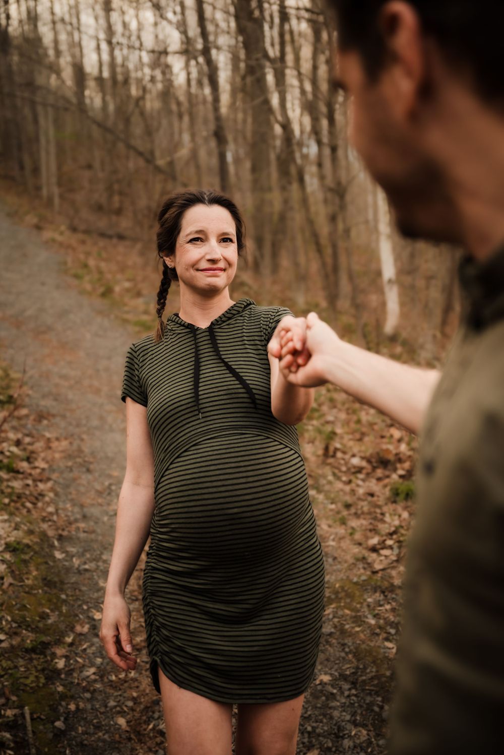Expectant couple holding hands on an autumn forest trail.