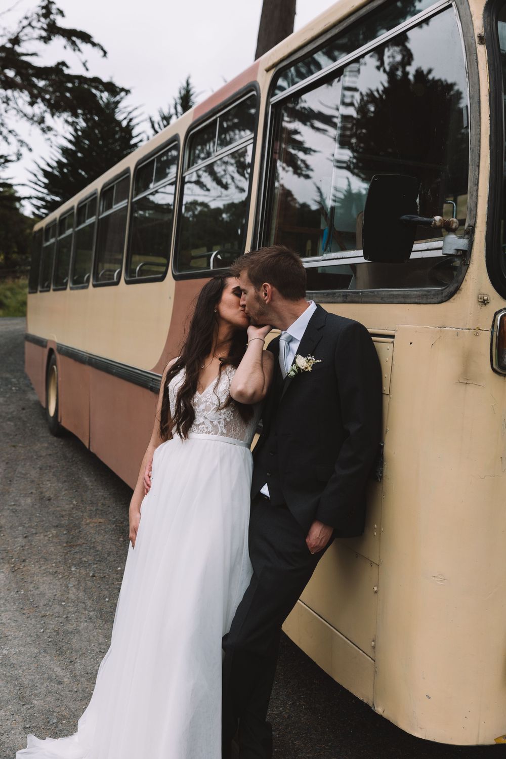 A romantic wedding moment shared against a vintage cream-colored bus backdrop.