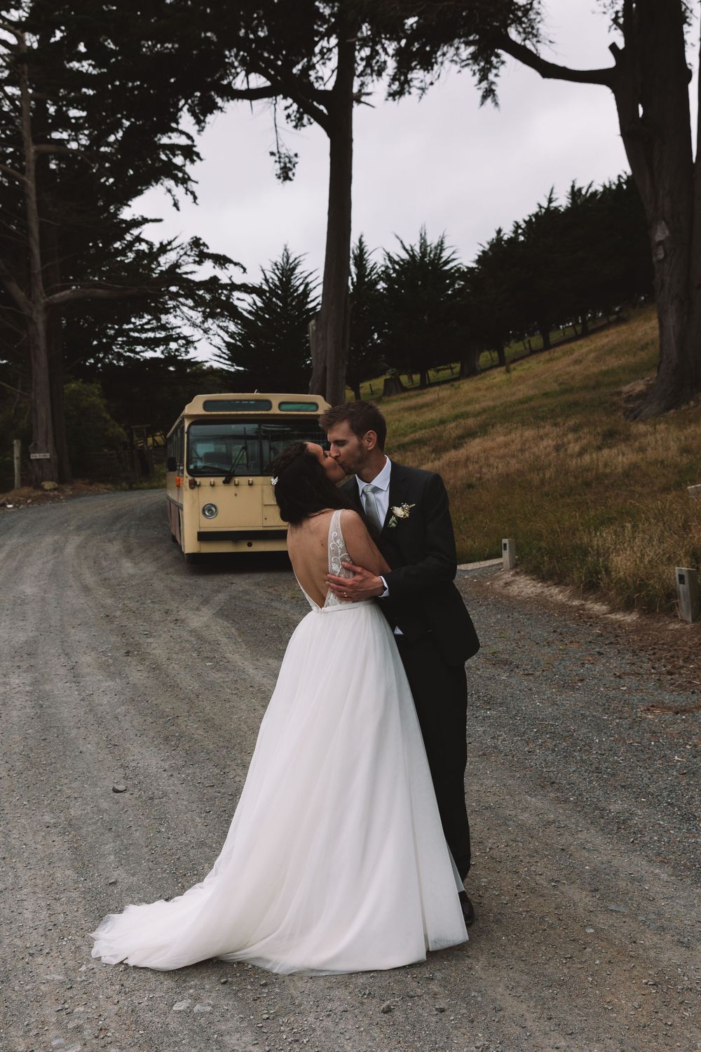 A romantic wedding portrait on a country road with a vintage bus in the background.