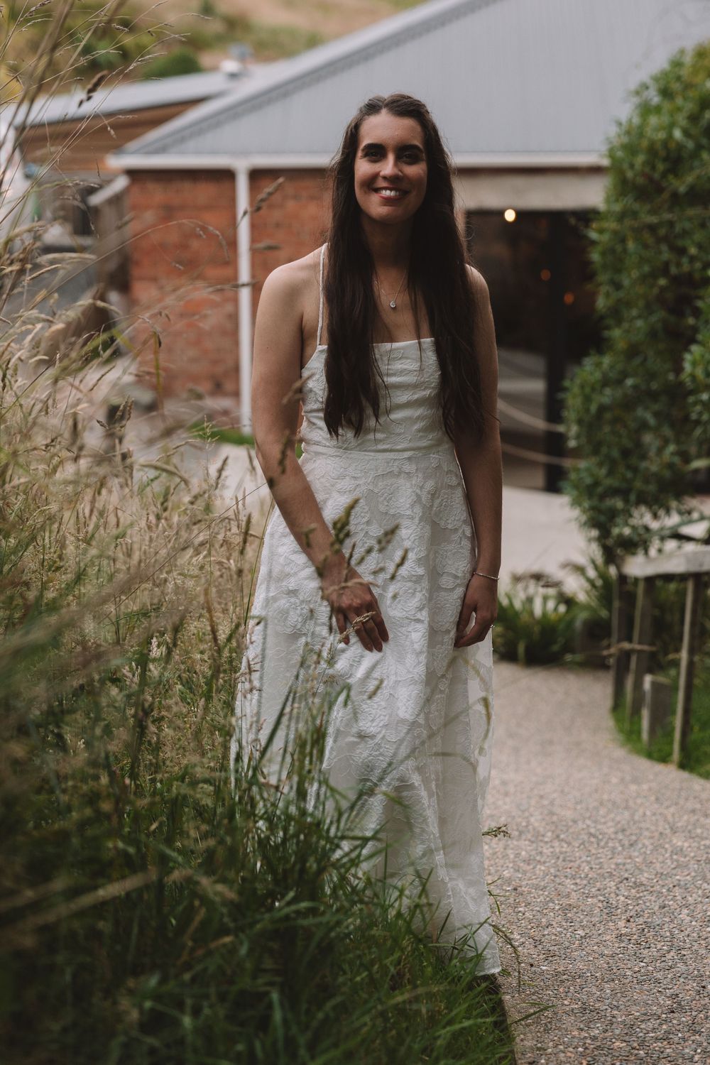 A beautiful lace wedding dress is worn gracefully on a garden pathway lined with ornamental grasses.