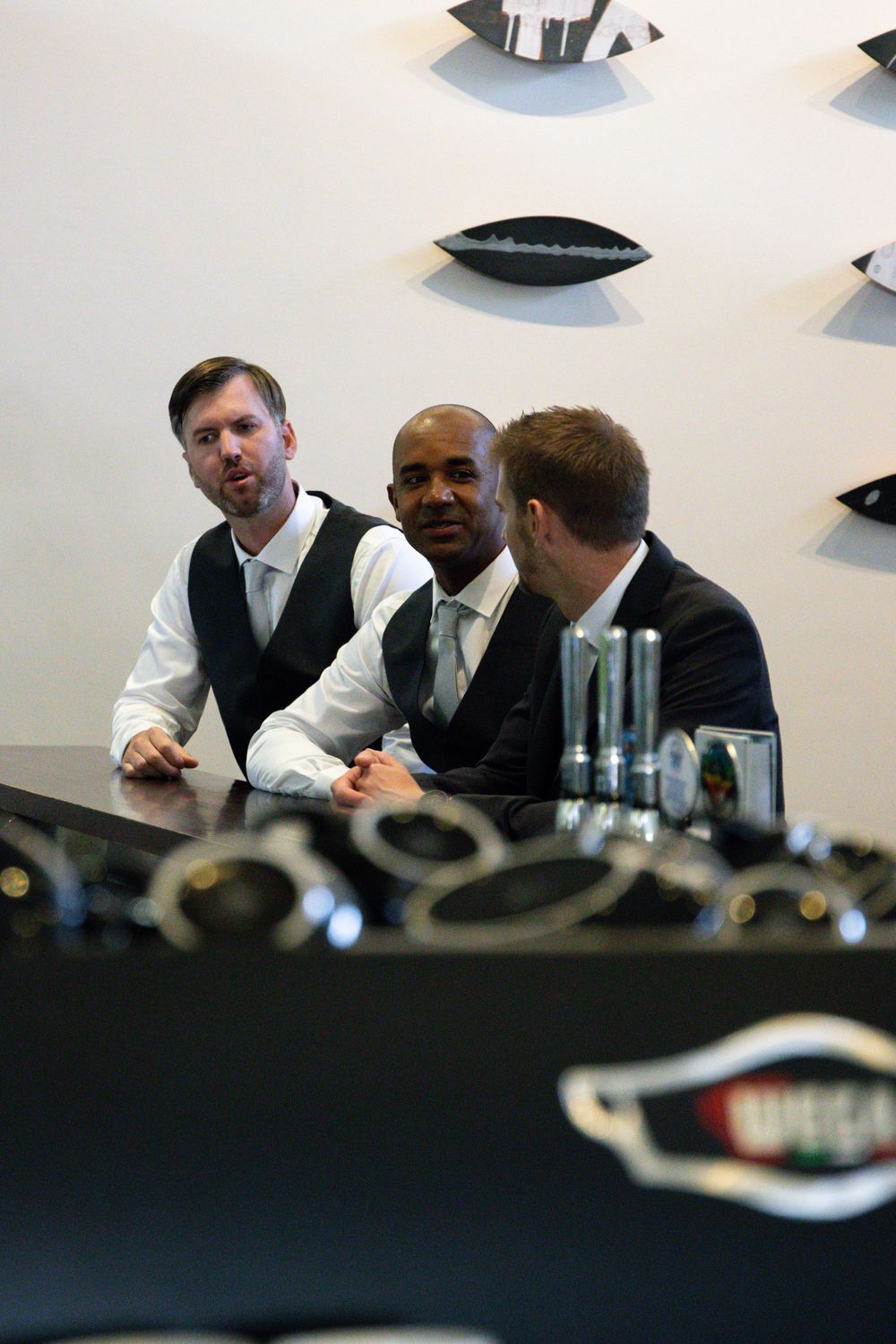 Three people in formal attire seated at a modern table with decorative wall art.
