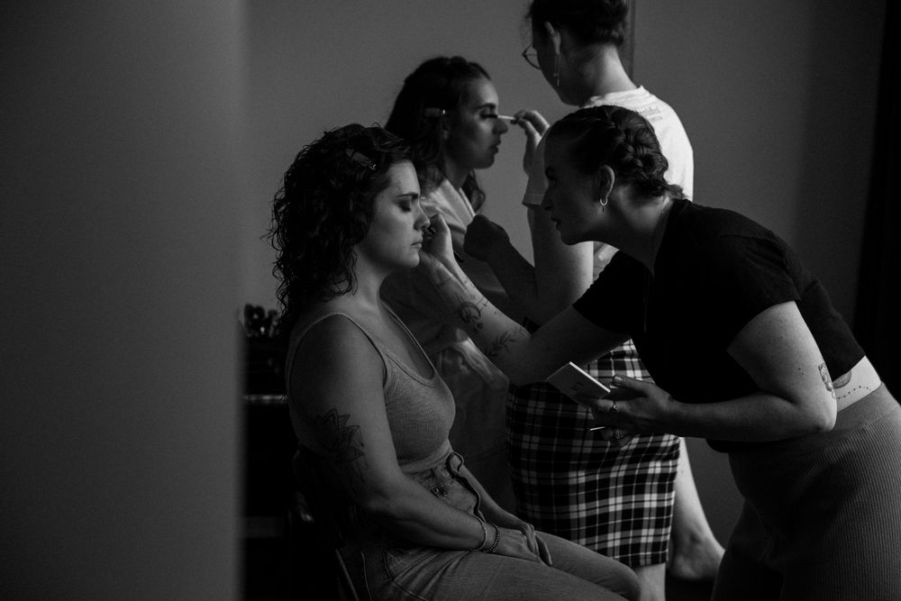 Professional makeup application during wedding preparations in moody lighting.