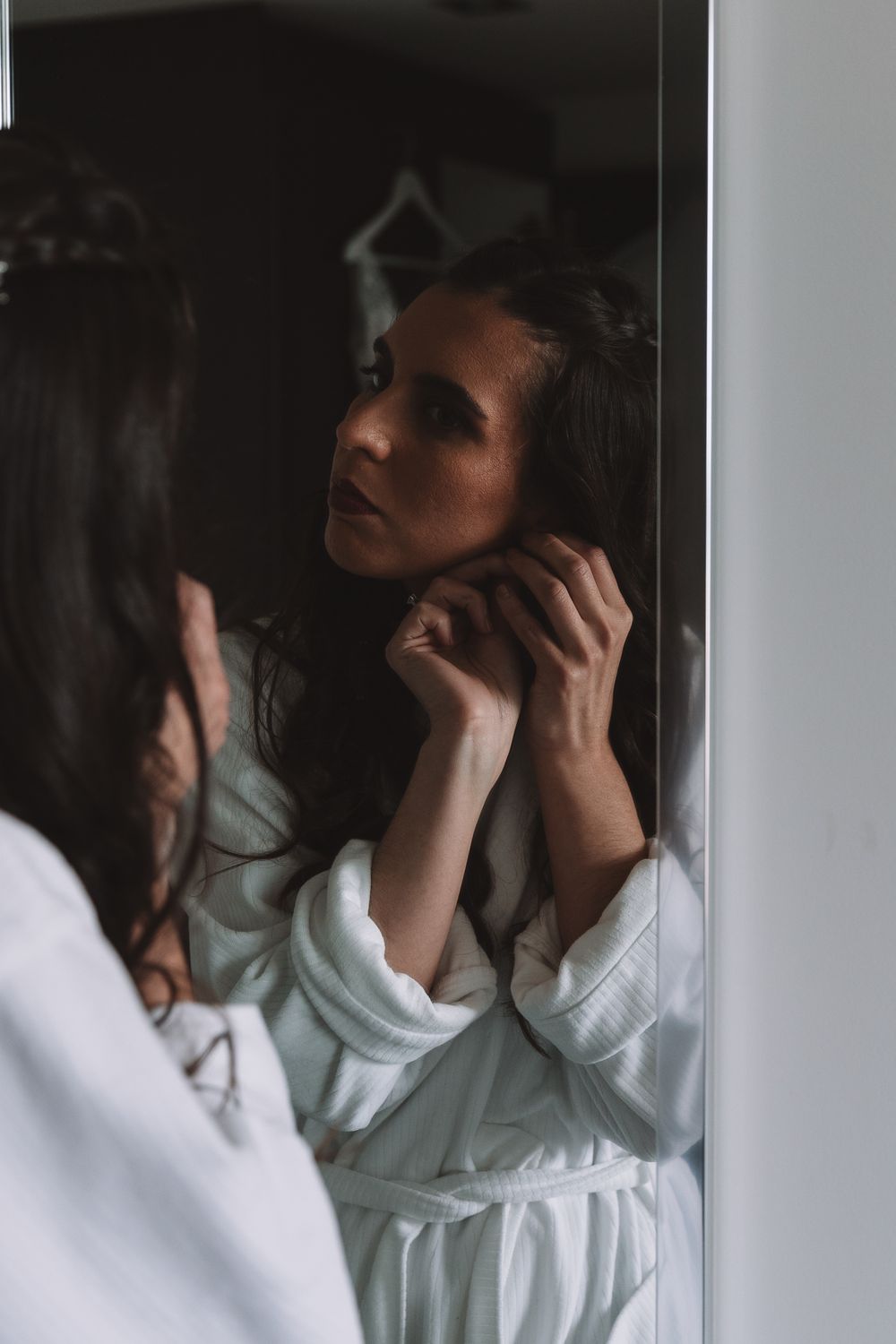 A reflection in a mirror shows someone adjusting their hair while wearing a white robe.
